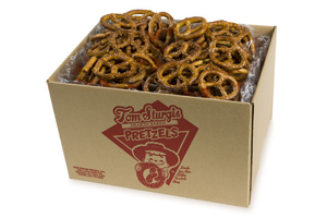 Open cardboard box containing brown pretzels. The side of the box has red printed text and a logo.
