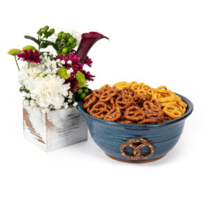 Blue ceramic bowl decorated with a pretzel design, filled with salted mini pretzels with a white wood box of flowers next to the bowl.