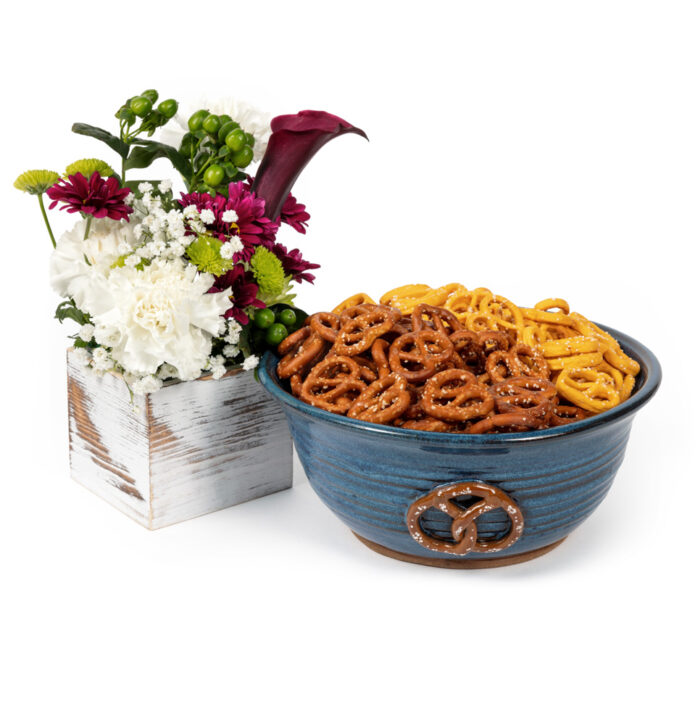 Blue ceramic bowl decorated with a pretzel design, filled with salted mini pretzels with a white wood box of flowers next to the bowl.